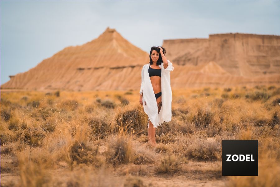 brunette female model posing in black bathing suit and white open shirt in the desert. Represented by a Las Vegas Modeling Agency.