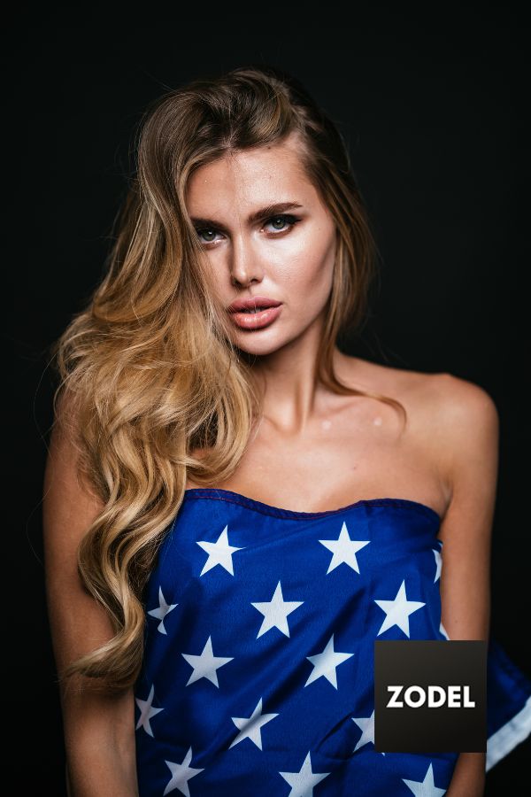 Beautiful blonde woman represented by a model agency, wrapped in the flag of the united states of america smiling. 